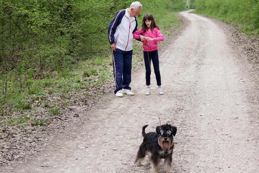 older man and young girl walking a dog on unpaved road
